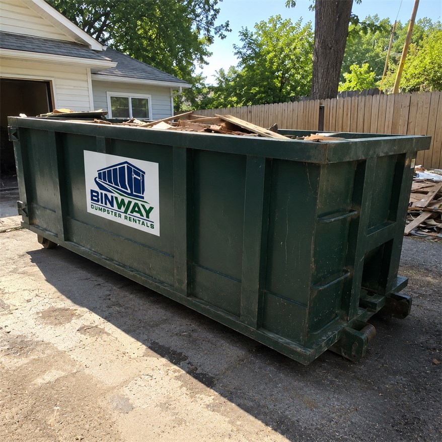 Dumpster filled with timber and demolition debris beside a fence on a construction site