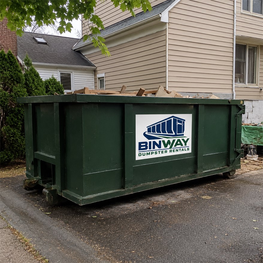 Roll-off dumpster loaded with lumber and construction offcuts on a residential driveway