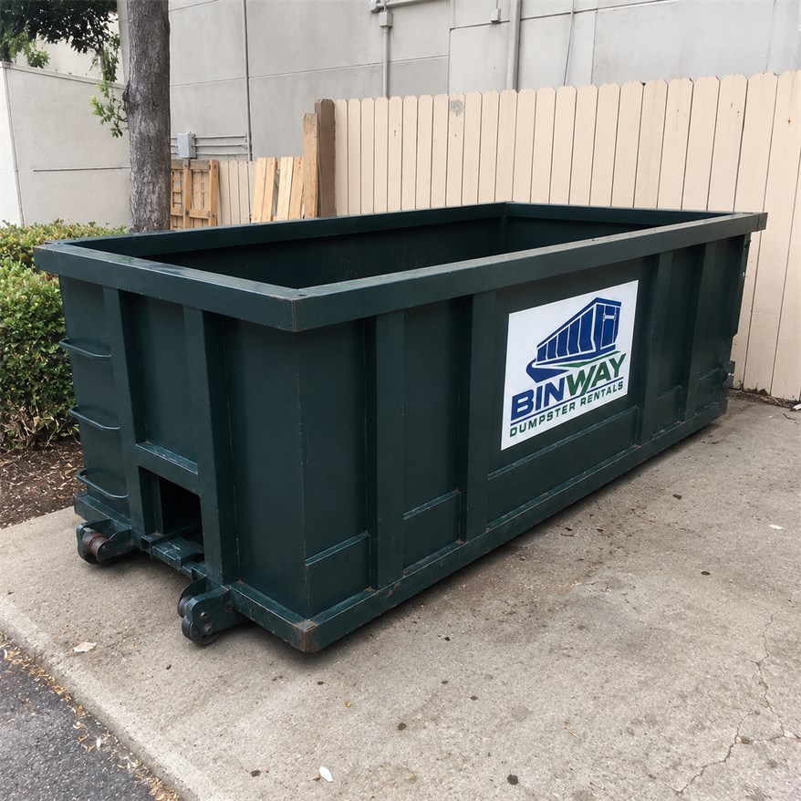 Green Binway roll-off dumpster placed beside a fence, ready for loading